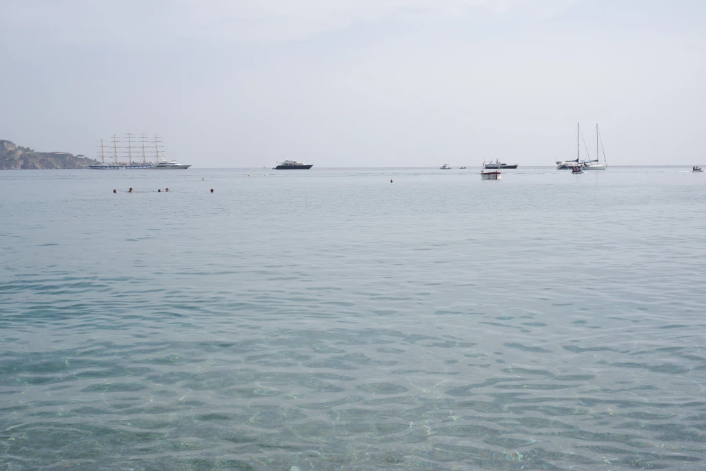Mare limpido di Giardini Naxos con grandi imbarcazioni all'orizzonte